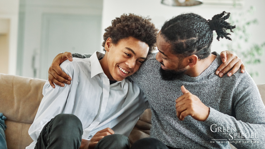 Father and son sitting on couch smiling at each other. 